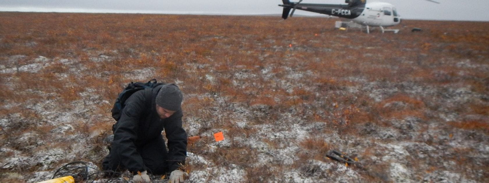 Grad student in arctic fieldwith helicopter in the background